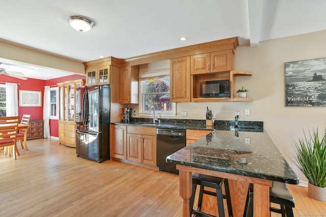 kitchen with a sink, light wood-style floors, black appliances, a peninsula, and a breakfast bar area