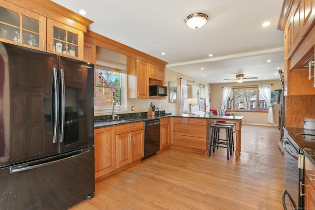 kitchen with a sink, black appliances, light wood-style floors, glass insert cabinets, and a peninsula