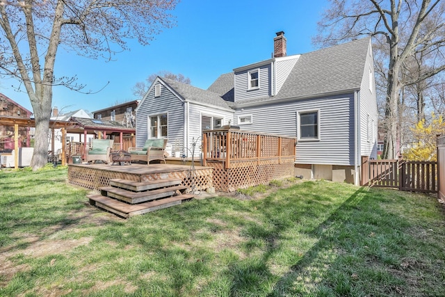 rear view of property featuring a lawn, a chimney, fence, a wooden deck, and roof with shingles
