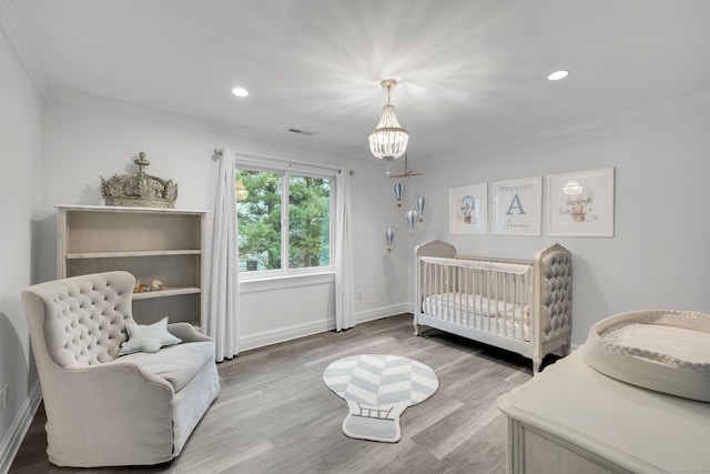 bedroom with crown molding, a nursery area, visible vents, a chandelier, and wood finished floors