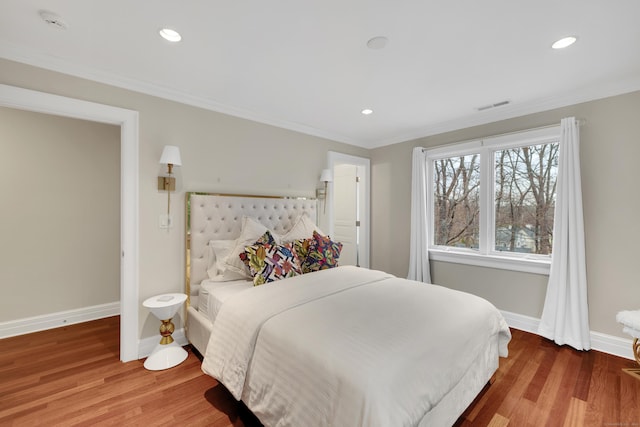 bedroom with crown molding, visible vents, baseboards, and wood finished floors