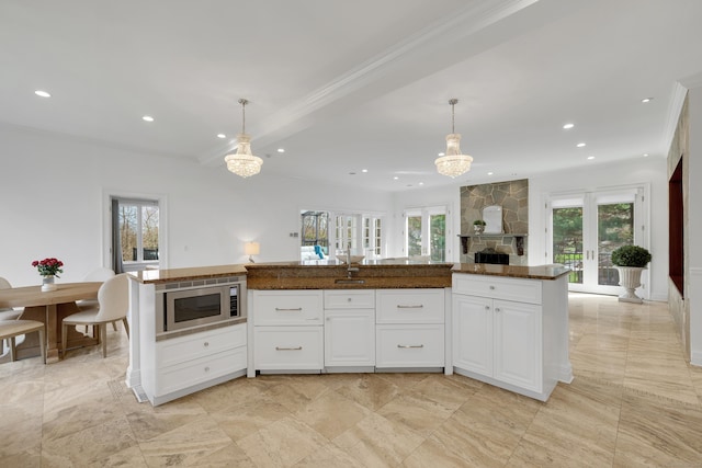kitchen featuring stainless steel microwave, a notable chandelier, a fireplace, white cabinetry, and crown molding