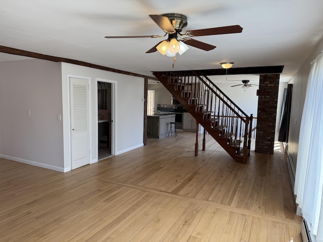 unfurnished living room featuring baseboard heating, stairs, light wood-type flooring, ceiling fan, and baseboards