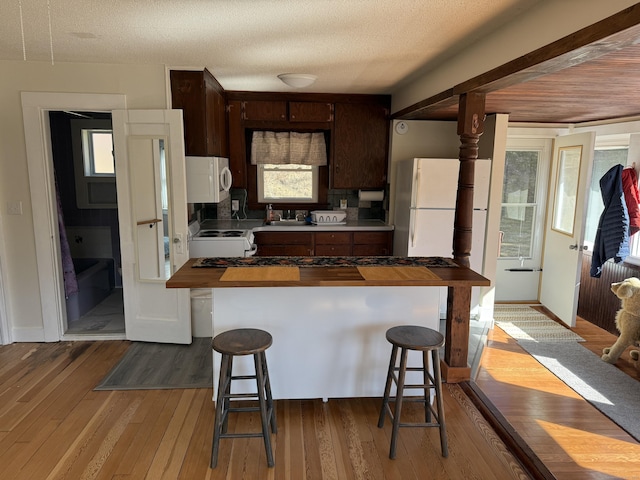 kitchen with white appliances, butcher block counters, dark brown cabinetry, a kitchen bar, and hardwood / wood-style flooring