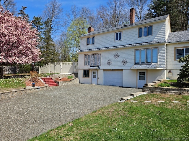 view of front of house with a chimney, an attached garage, driveway, and fence