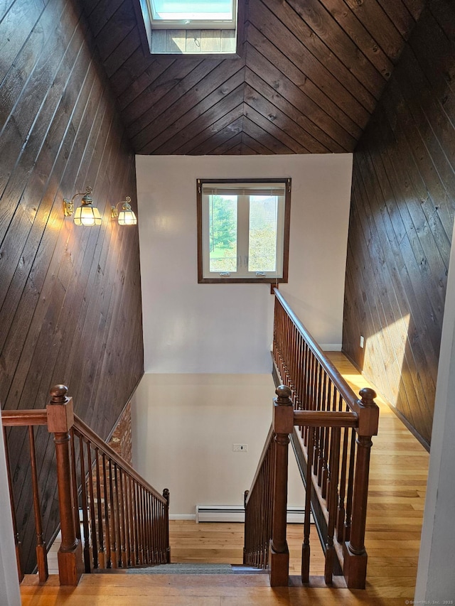 staircase with wood ceiling, baseboard heating, wood walls, and hardwood / wood-style flooring