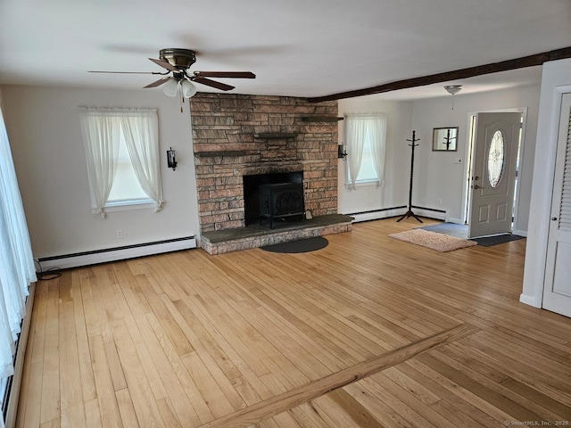 unfurnished living room with a baseboard heating unit, wood-type flooring, a wood stove, and a ceiling fan