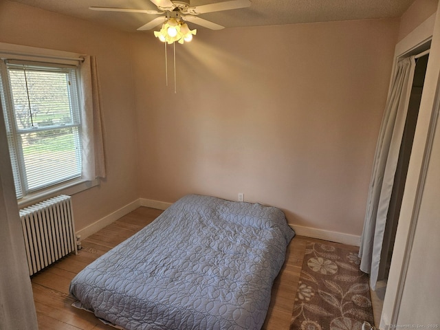 bedroom featuring ceiling fan, radiator heating unit, baseboards, and wood finished floors