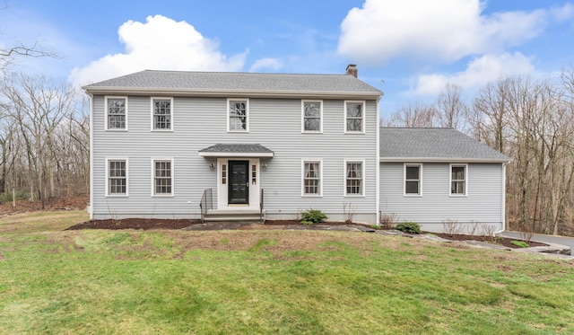 colonial inspired home with a chimney, a shingled roof, and a front yard