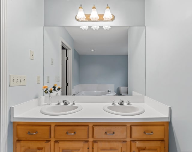 full bath featuring toilet, a bath, double vanity, and a sink