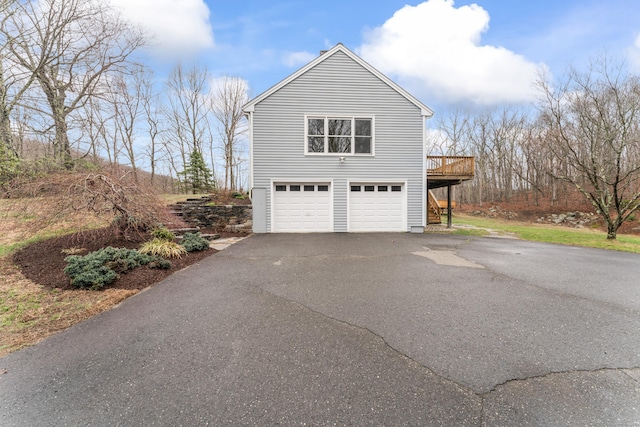 view of side of property with an attached garage, a wooden deck, and aphalt driveway