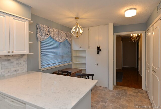 16 Heritage Vlg Unit A, Southbury, CT 06488 - kitchen featuring a chandelier, decorative backsplash, a peninsula, white cabinetry, and stone finish floors
