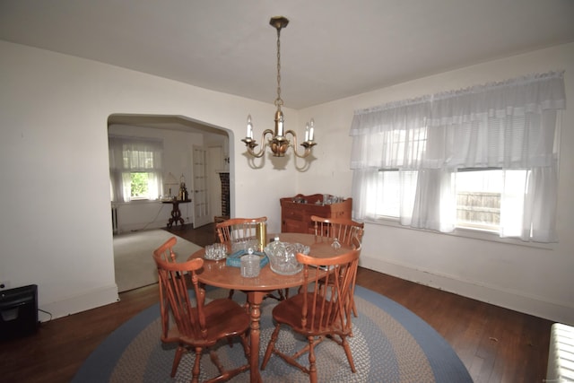 dining space featuring arched walkways, a chandelier, wood finished floors, baseboards, and radiator heating unit