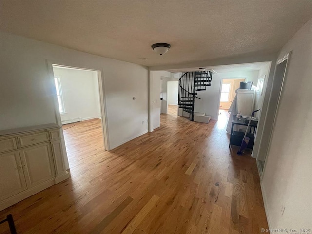 interior space with a baseboard radiator, light wood-type flooring, stairway, and a textured ceiling