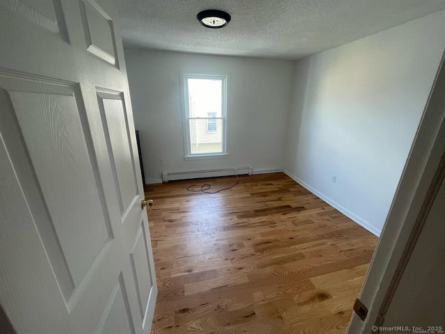 spare room featuring baseboard heating, a textured ceiling, baseboards, and wood finished floors