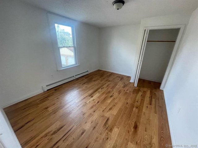unfurnished bedroom featuring light wood finished floors, baseboard heating, a textured ceiling, and baseboards