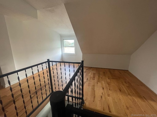 additional living space with a textured ceiling, wood finished floors, and lofted ceiling