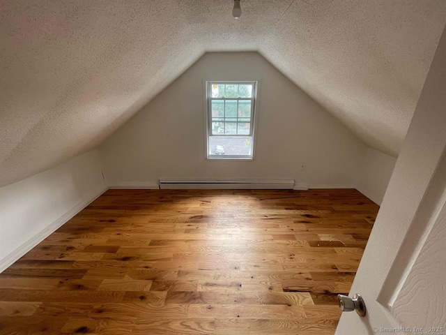 bonus room featuring a textured ceiling, vaulted ceiling, baseboard heating, wood finished floors, and baseboards