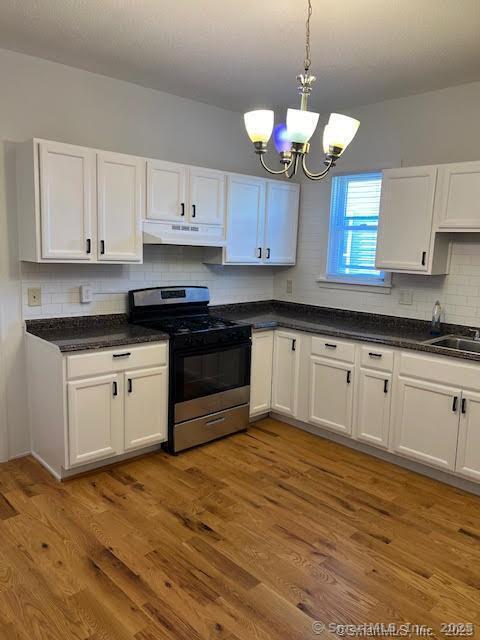 kitchen featuring under cabinet range hood, gas stove, white cabinetry, and an inviting chandelier