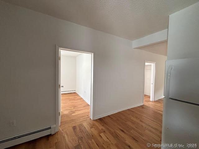 empty room featuring baseboard heating, wood finished floors, a baseboard heating unit, and baseboards