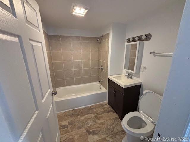 full bath with toilet, bathtub / shower combination, vanity, and stone finish flooring