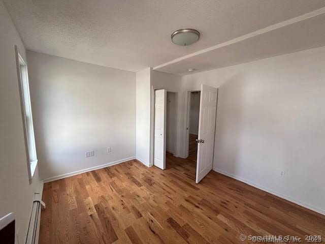 unfurnished bedroom with baseboard heating, a textured ceiling, wood finished floors, and baseboards