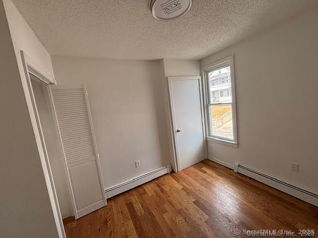 unfurnished bedroom featuring visible vents, a textured ceiling, wood finished floors, and baseboard heating