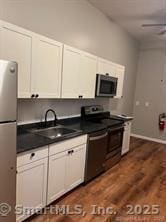 kitchen featuring white cabinetry, dark countertops, dark wood-type flooring, appliances with stainless steel finishes, and a sink