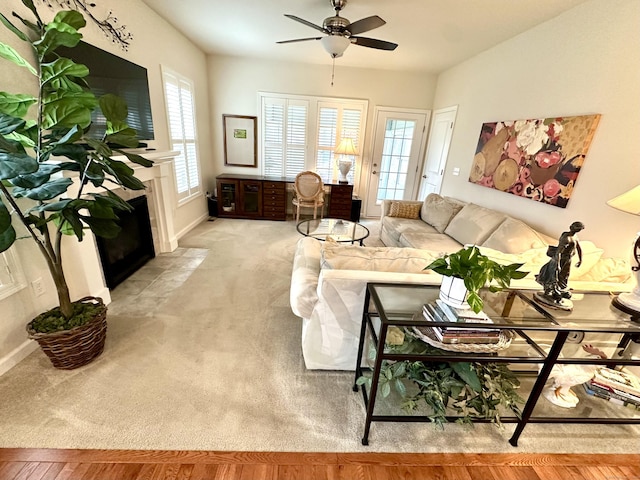 carpeted living area with a fireplace with flush hearth, a ceiling fan, and baseboards