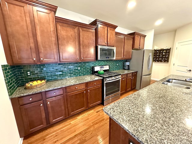 kitchen with light wood-style flooring, a sink, backsplash, light stone countertops, and appliances with stainless steel finishes