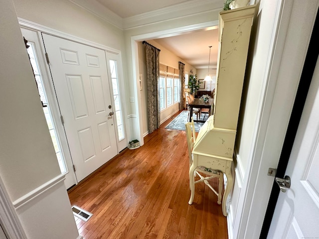 foyer entrance with crown molding, light wood-style floors, and visible vents