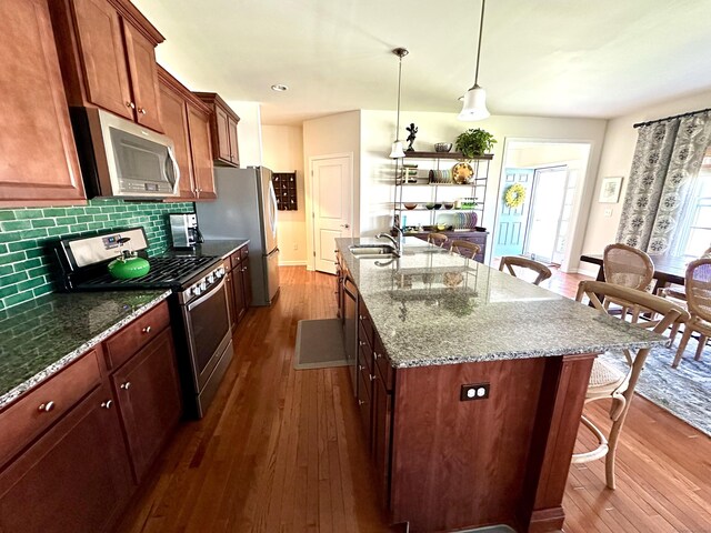 kitchen featuring dark wood finished floors, a sink, tasteful backsplash, appliances with stainless steel finishes, and a breakfast bar area