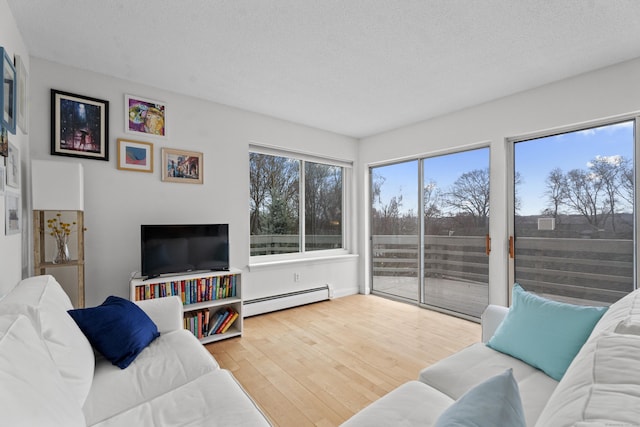 living area with baseboard heating, a textured ceiling, wood finished floors, and a wealth of natural light