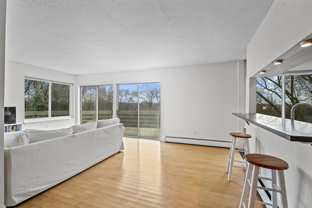 living area with baseboard heating, a textured ceiling, and light wood-style flooring