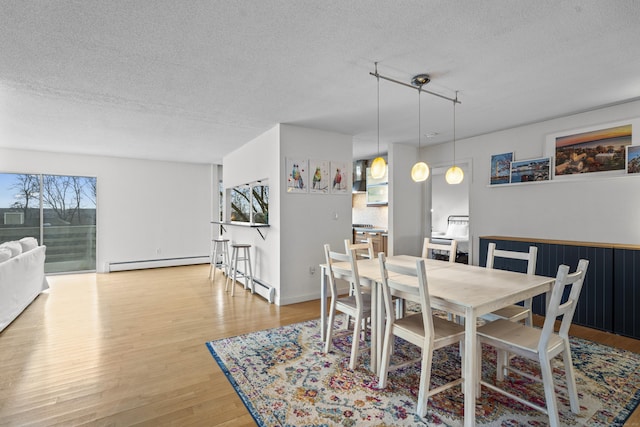 dining room with a baseboard heating unit, a textured ceiling, and wood finished floors