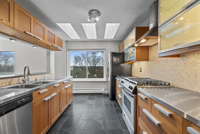 kitchen with wall chimney range hood, a skylight, appliances with stainless steel finishes, stainless steel counters, and a baseboard heating unit