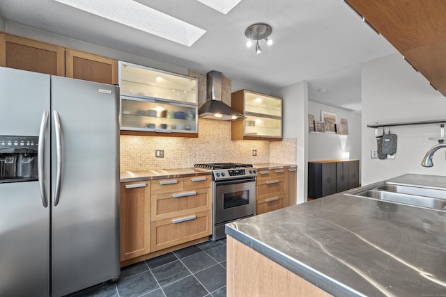 kitchen with a sink, wall chimney range hood, appliances with stainless steel finishes, stainless steel countertops, and a skylight