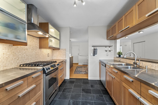 kitchen featuring wall chimney exhaust hood, tasteful backsplash, appliances with stainless steel finishes, a sink, and brown cabinets