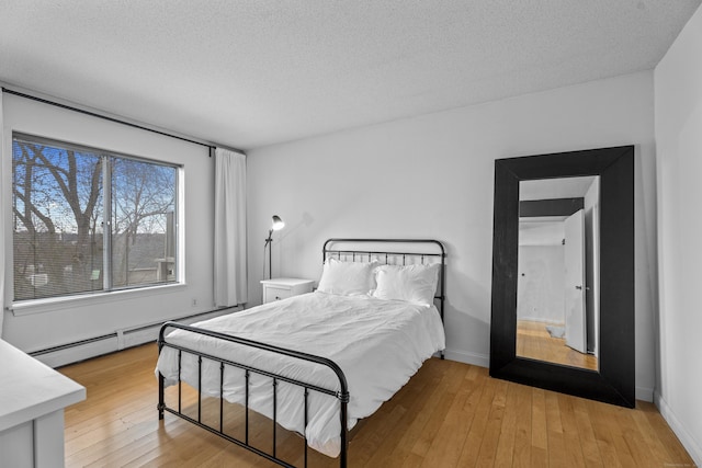 bedroom with baseboards, light wood-style floors, a baseboard radiator, and a textured ceiling