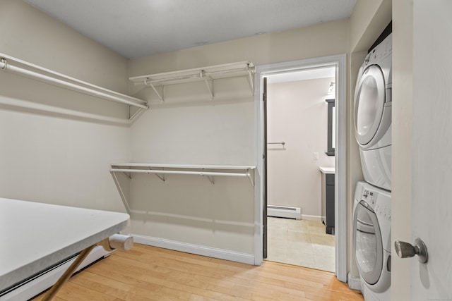 washroom with baseboards, light wood-type flooring, laundry area, baseboard heating, and stacked washer and dryer