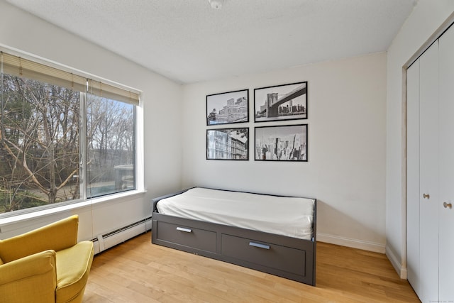 bedroom with baseboard heating, a closet, light wood finished floors, and baseboards