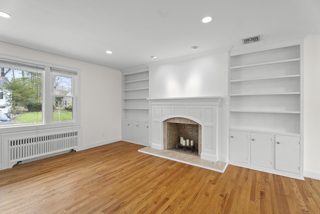 unfurnished living room featuring recessed lighting, built in shelves, light wood-style flooring, and radiator
