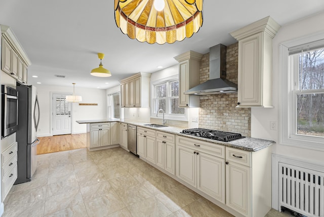 kitchen with cream cabinets, wall chimney exhaust hood, radiator, stainless steel appliances, and a sink