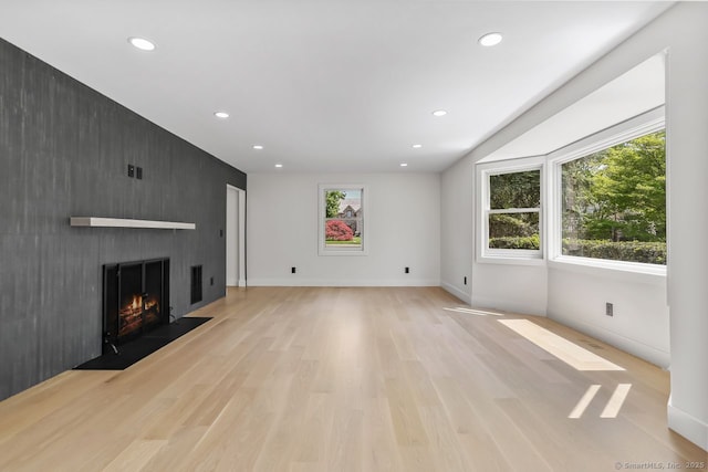 unfurnished living room with healthy amount of natural light, recessed lighting, light wood-style floors, a large fireplace, and baseboards