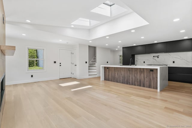 unfurnished living room with a skylight, stairway, light wood-style floors, recessed lighting, and baseboards