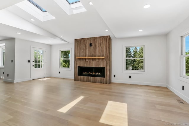 unfurnished living room with a skylight, a large fireplace, light wood-style flooring, recessed lighting, and vaulted ceiling