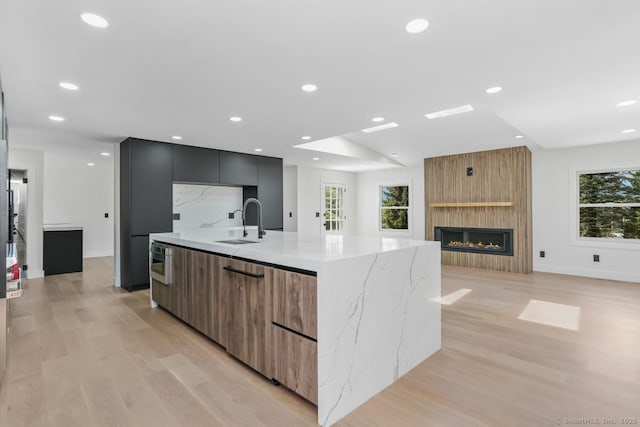 kitchen featuring modern cabinets, a sink, a large island, light wood finished floors, and light stone counters