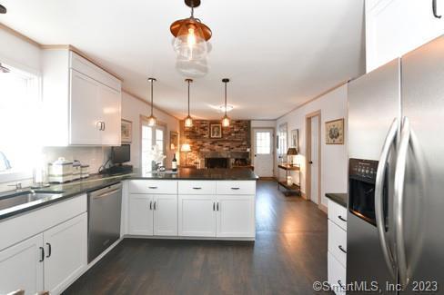 kitchen with a sink, dark wood-type flooring, a peninsula, dark countertops, and appliances with stainless steel finishes