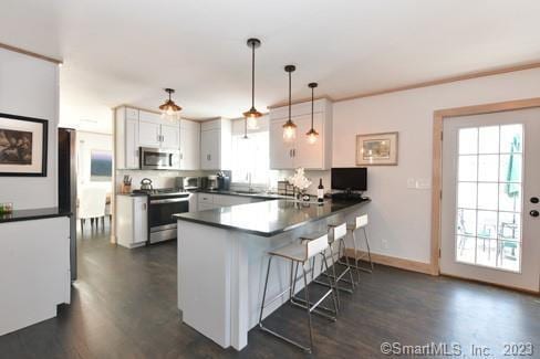 kitchen with a breakfast bar, stainless steel appliances, dark countertops, white cabinetry, and a peninsula