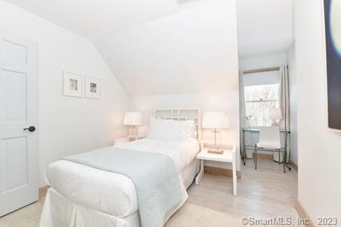 bedroom with vaulted ceiling, wood finished floors, and baseboards